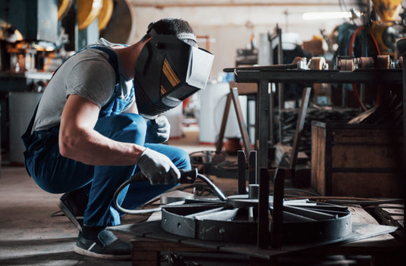 Portrait of a young worker at a large metalworking plant. The welder engineer works in a protective mask